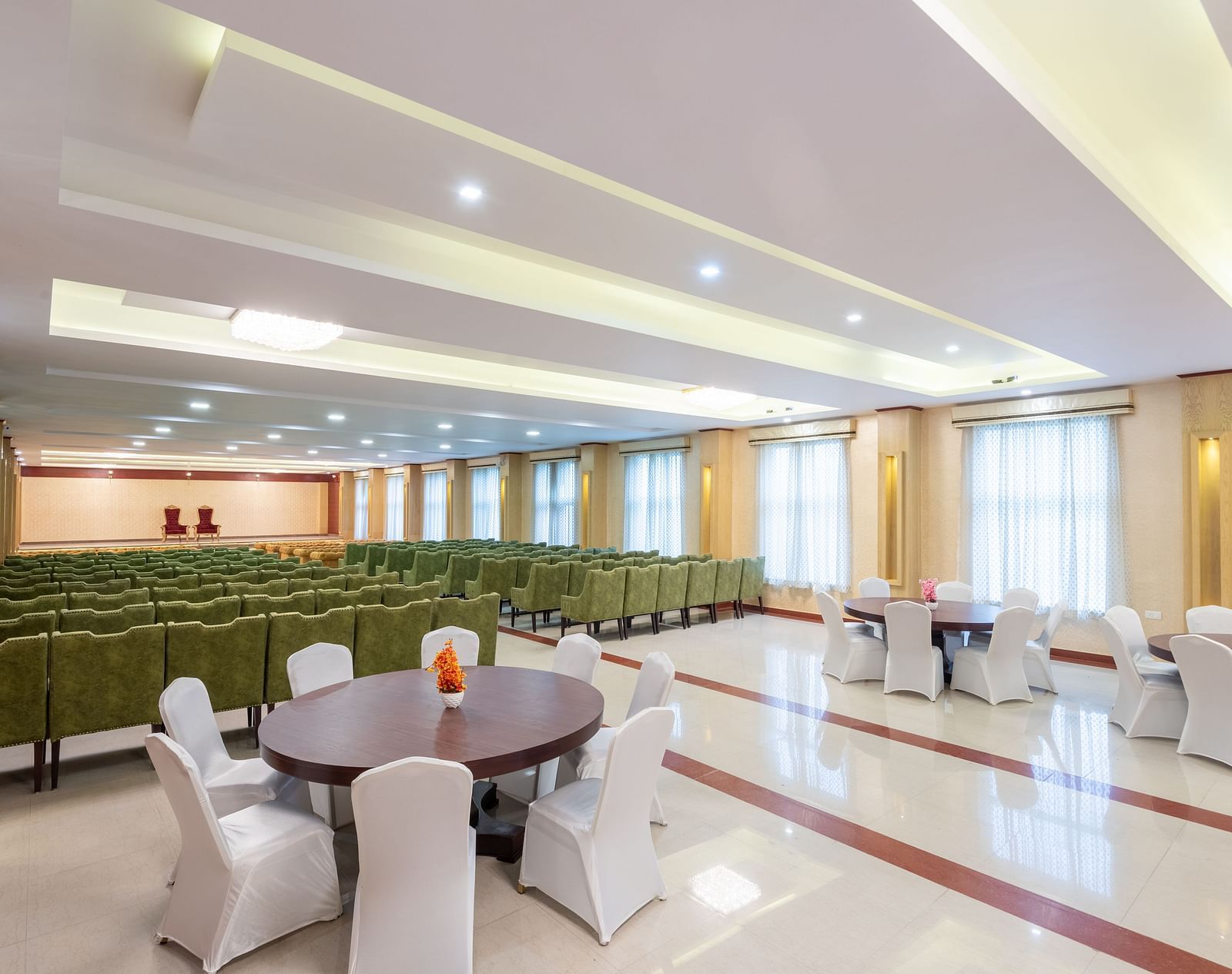 A side angle shot of a banquet hall at DLS Tehri Club Resort featuring green sofas and round table.